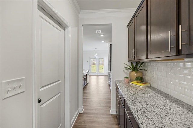 kitchen featuring hardwood / wood-style flooring, ornamental molding, dark brown cabinetry, light stone counters, and tasteful backsplash