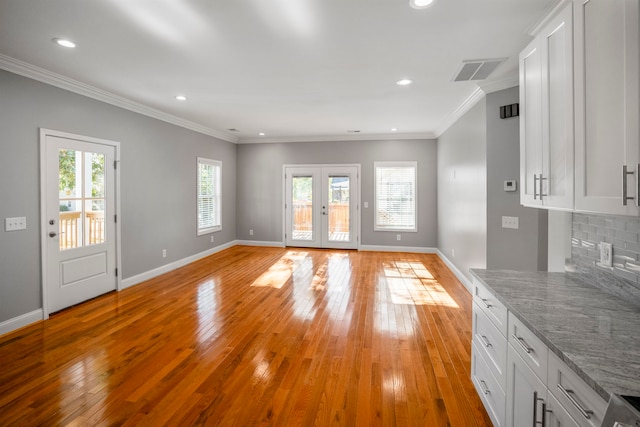 unfurnished living room featuring french doors, ornamental molding, and light wood-type flooring