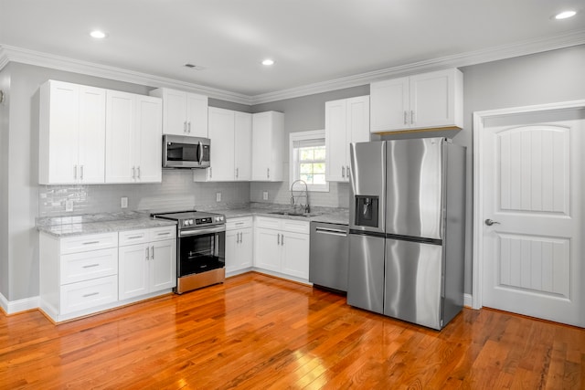 kitchen featuring appliances with stainless steel finishes, sink, white cabinetry, crown molding, and light hardwood / wood-style flooring