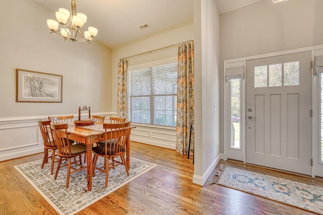 dining area with an inviting chandelier, hardwood / wood-style floors, a healthy amount of sunlight, and vaulted ceiling