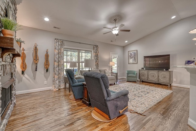 living room featuring a stone fireplace, lofted ceiling, hardwood / wood-style floors, and ceiling fan