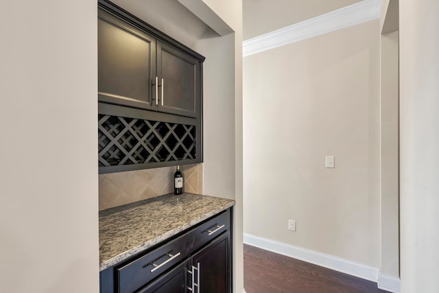 bar featuring dark brown cabinets, backsplash, dark wood-type flooring, crown molding, and light stone counters