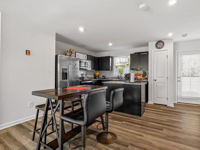 kitchen with appliances with stainless steel finishes, dark hardwood / wood-style floors, a kitchen bar, and a kitchen island