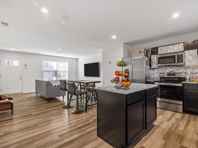 kitchen featuring a kitchen island, decorative backsplash, stainless steel appliances, light stone countertops, and light wood-type flooring