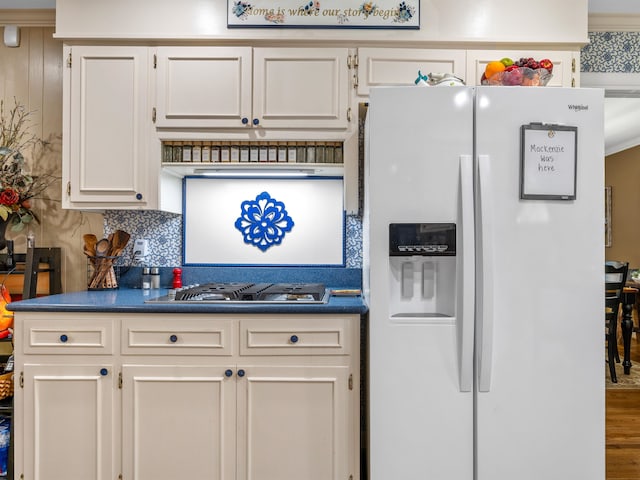 kitchen with stainless steel gas cooktop, backsplash, white refrigerator with ice dispenser, hardwood / wood-style floors, and crown molding