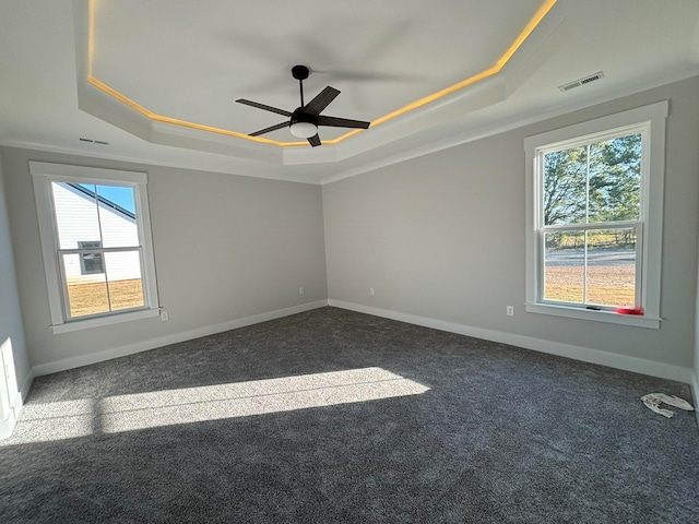 empty room featuring dark colored carpet, ceiling fan, a healthy amount of sunlight, and a raised ceiling