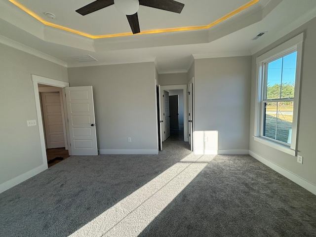 unfurnished bedroom featuring ceiling fan, a raised ceiling, ornamental molding, and dark carpet