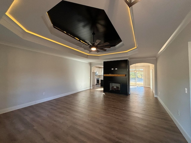 unfurnished living room with ornamental molding, dark hardwood / wood-style floors, a tray ceiling, and ceiling fan