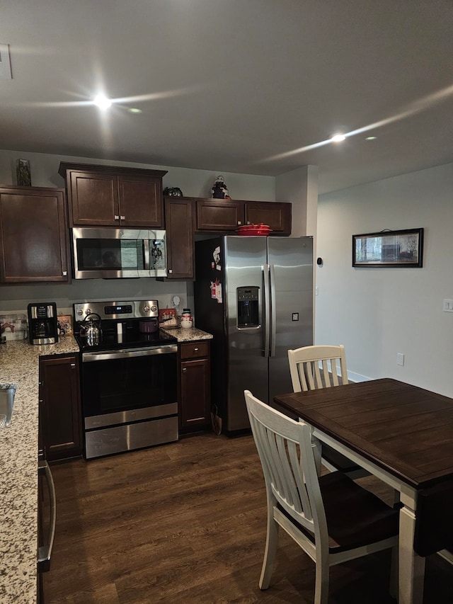 kitchen with dark brown cabinets, stainless steel appliances, dark hardwood / wood-style floors, and light stone countertops