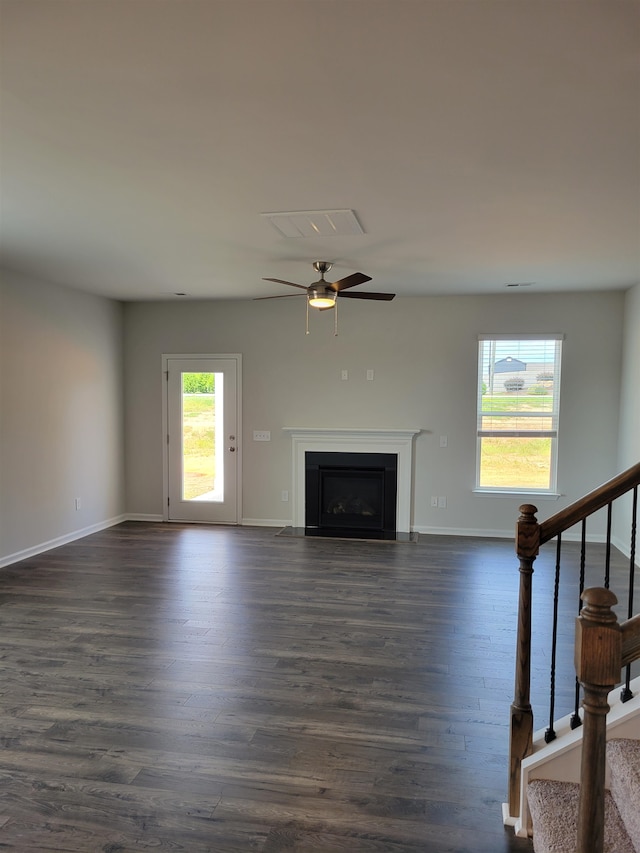 unfurnished living room featuring a healthy amount of sunlight, dark wood-type flooring, and ceiling fan