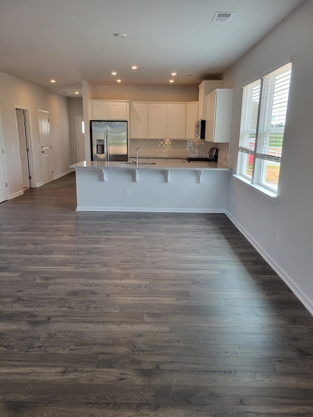 kitchen featuring light stone countertops, appliances with stainless steel finishes, kitchen peninsula, white cabinets, and dark hardwood / wood-style floors