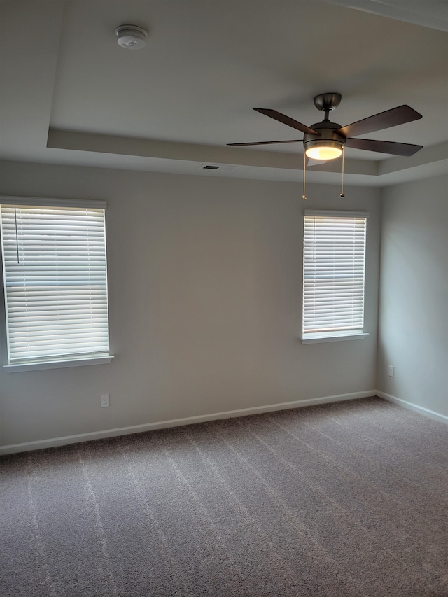 empty room featuring a raised ceiling, carpet floors, and ceiling fan