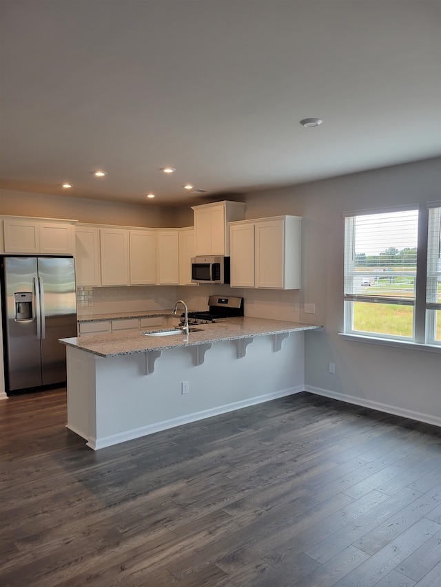 kitchen featuring sink, stainless steel appliances, white cabinets, dark wood-type flooring, and a breakfast bar