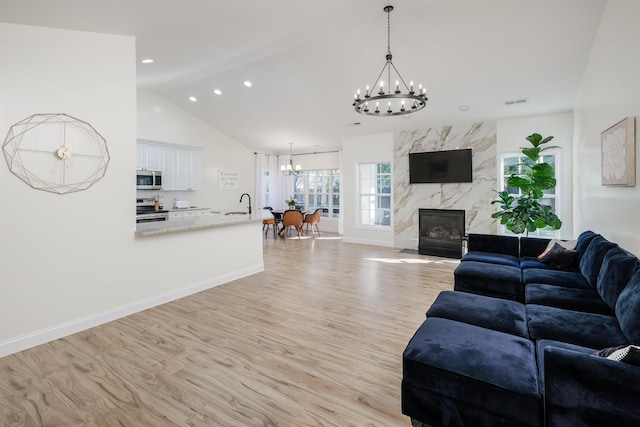 living room with light hardwood / wood-style floors, sink, a fireplace, and vaulted ceiling