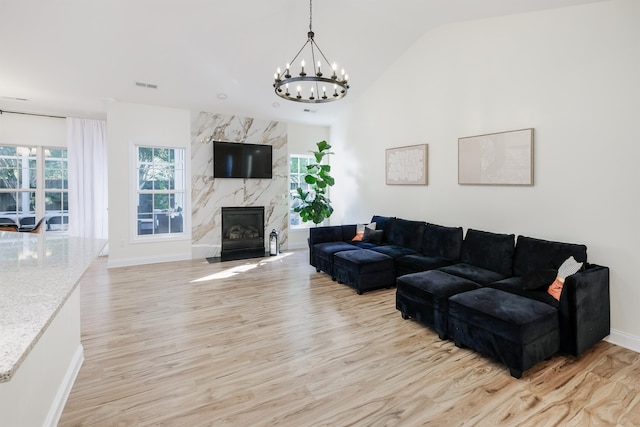 living room featuring light hardwood / wood-style floors, a notable chandelier, vaulted ceiling, and a high end fireplace