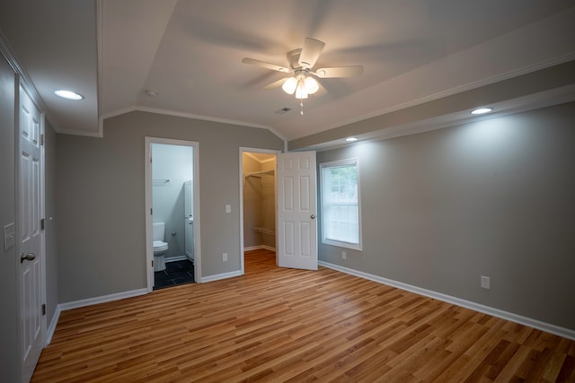 unfurnished bedroom featuring wood-type flooring, a walk in closet, a closet, ceiling fan, and ornamental molding