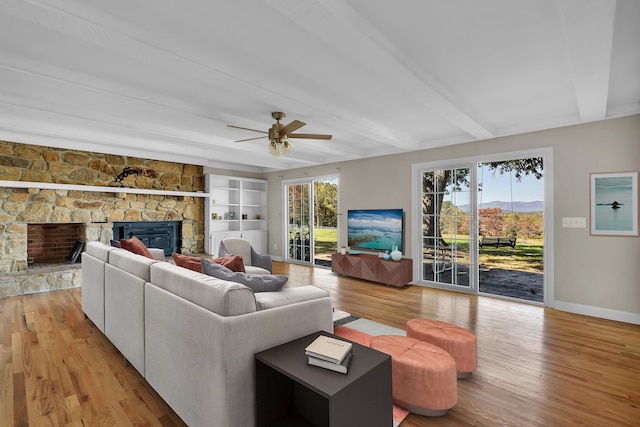 living room with beam ceiling, a healthy amount of sunlight, a fireplace, and light wood-type flooring