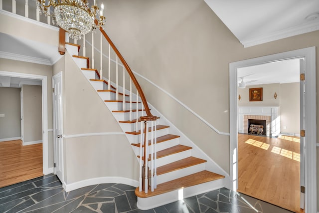 stairway with wood-type flooring, vaulted ceiling, a brick fireplace, ornamental molding, and a notable chandelier