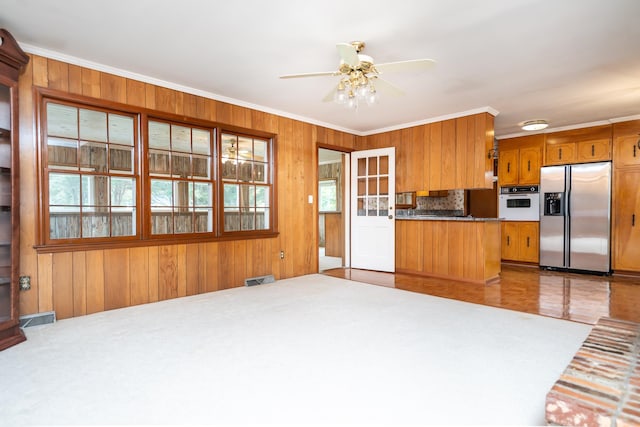 kitchen featuring white oven, stainless steel refrigerator with ice dispenser, backsplash, ornamental molding, and wood walls