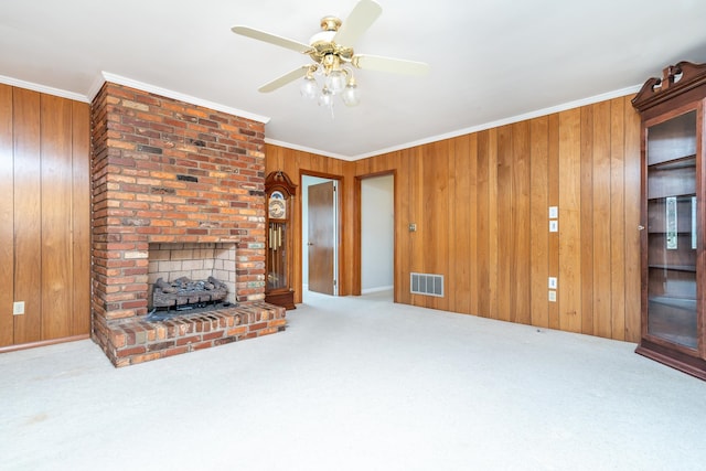 unfurnished living room with crown molding, ceiling fan, a fireplace, and wooden walls