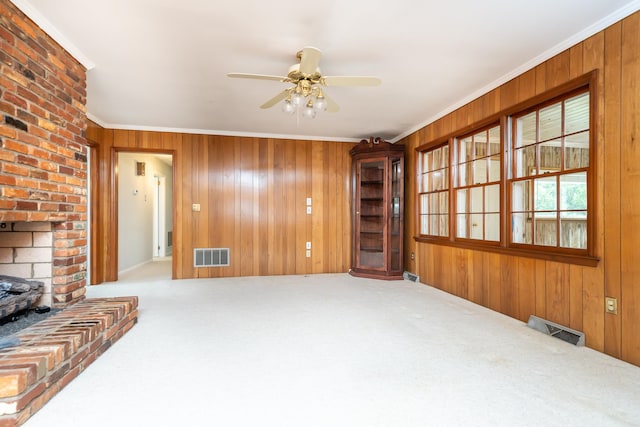 living room with wood walls, a brick fireplace, ceiling fan, ornamental molding, and light colored carpet