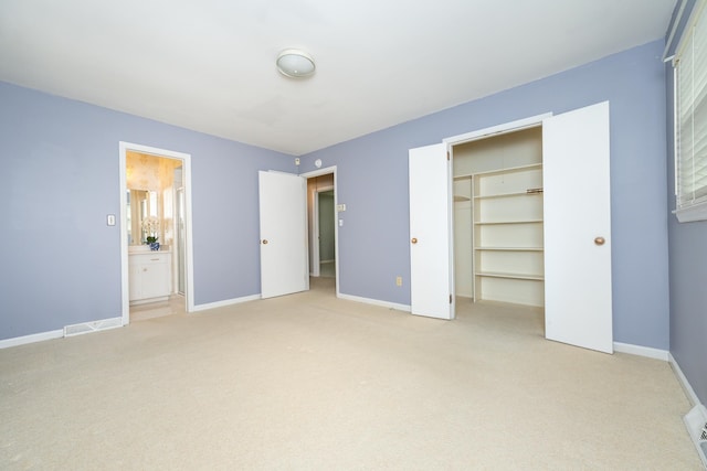 unfurnished bedroom with light carpet, a closet, and ensuite bath