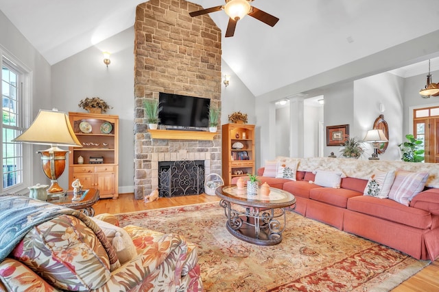 living room with ceiling fan, high vaulted ceiling, light hardwood / wood-style flooring, ornate columns, and a stone fireplace