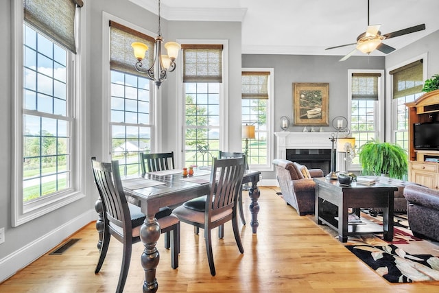 dining room with light wood-type flooring, crown molding, plenty of natural light, and ceiling fan with notable chandelier