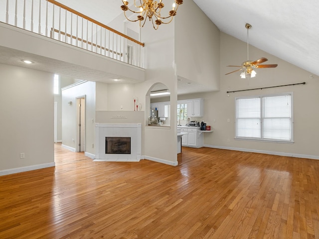 unfurnished living room featuring light hardwood / wood-style floors, a tiled fireplace, high vaulted ceiling, and ceiling fan with notable chandelier