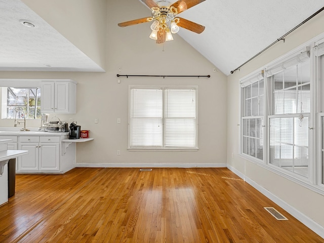 interior space featuring light wood-type flooring, a textured ceiling, white cabinetry, ceiling fan, and high vaulted ceiling