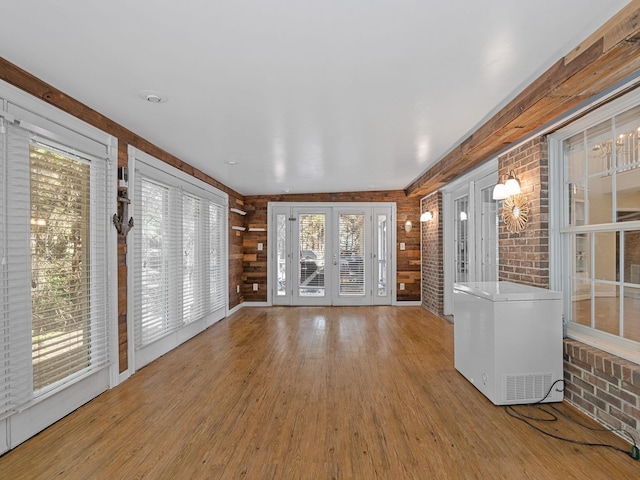 unfurnished living room with a healthy amount of sunlight, hardwood / wood-style flooring, and brick wall