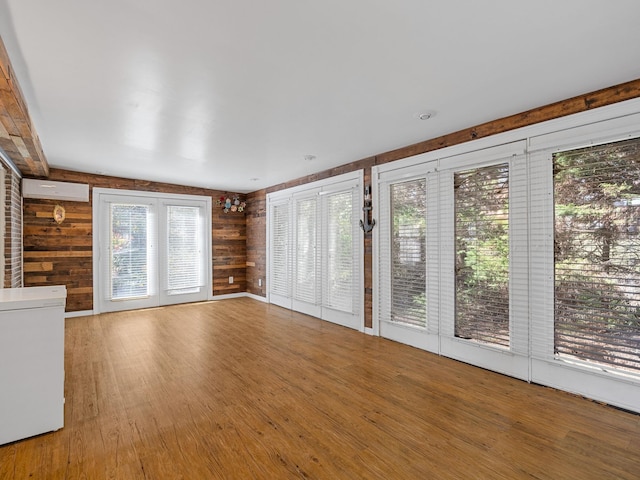 unfurnished living room with an AC wall unit, wood-type flooring, and wooden walls