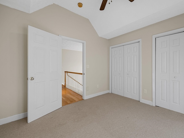 unfurnished bedroom featuring ceiling fan, carpet flooring, lofted ceiling, and two closets