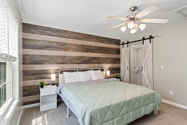 bedroom featuring wooden walls, a barn door, and ceiling fan