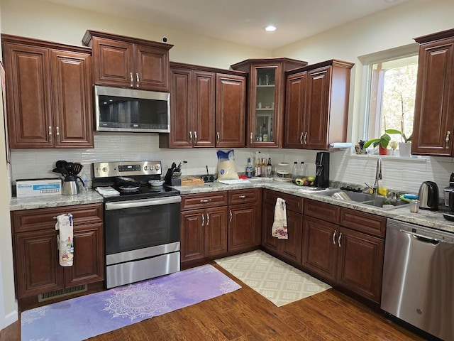 kitchen featuring tasteful backsplash, light stone counters, sink, light hardwood / wood-style floors, and stainless steel appliances