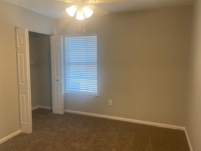 unfurnished bedroom with a closet, dark carpet, and ceiling fan