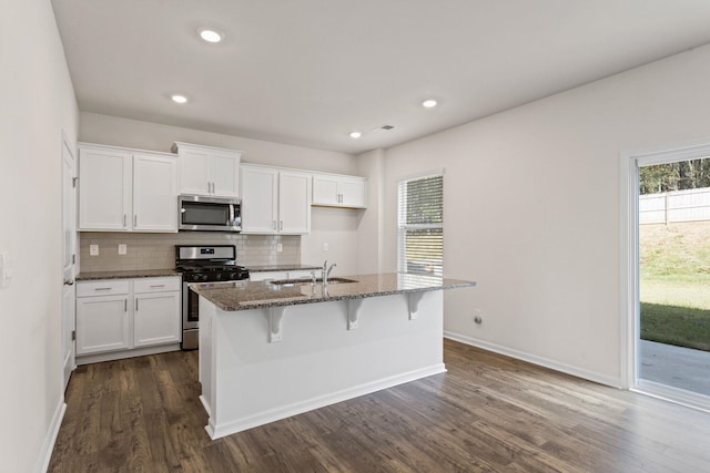 kitchen featuring dark hardwood / wood-style floors, stainless steel appliances, dark stone countertops, a center island with sink, and white cabinetry