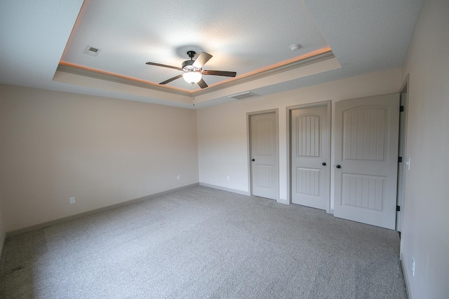 unfurnished bedroom with multiple closets, carpet floors, ceiling fan, and a tray ceiling