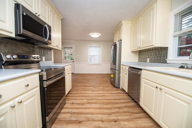 kitchen with sink, appliances with stainless steel finishes, light hardwood / wood-style flooring, cream cabinetry, and decorative backsplash