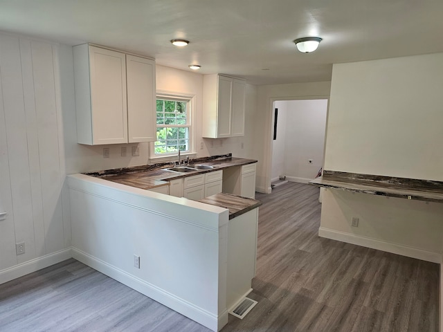 kitchen featuring wood-type flooring, white cabinetry, sink, and kitchen peninsula