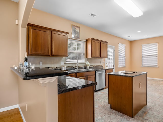 kitchen featuring kitchen peninsula, dark stone counters, sink, and dishwasher