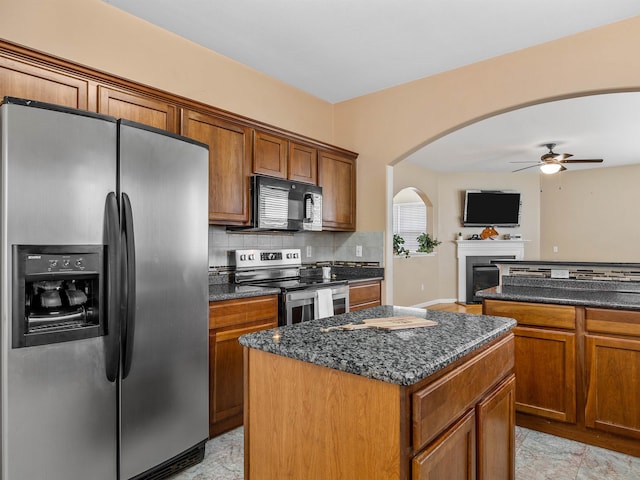 kitchen featuring stainless steel appliances, a center island, ceiling fan, backsplash, and dark stone countertops