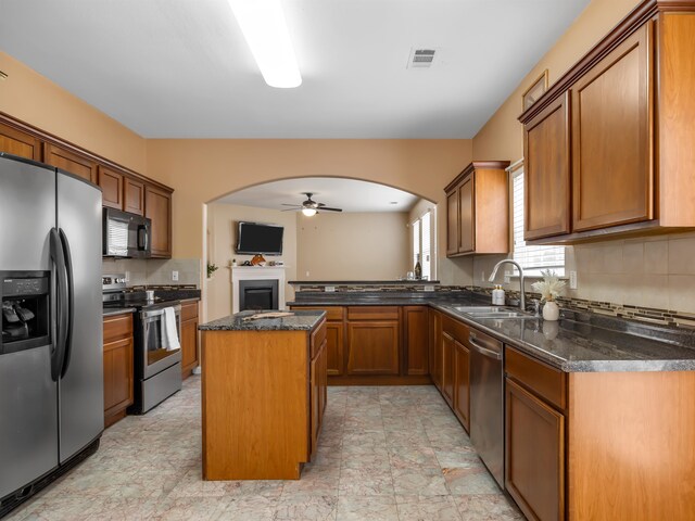 kitchen featuring stainless steel appliances, sink, dark stone countertops, ceiling fan, and a center island