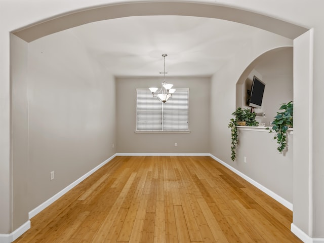 spare room with hardwood / wood-style floors and an inviting chandelier