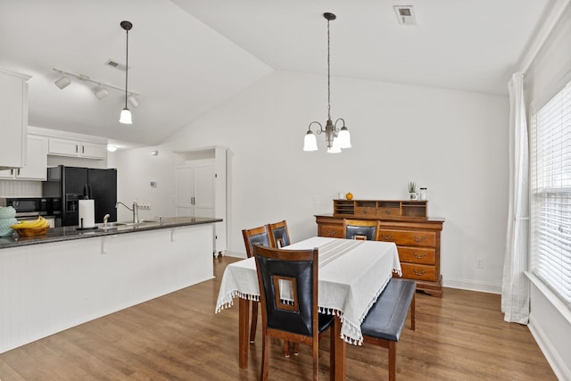 dining space featuring rail lighting, wood-type flooring, vaulted ceiling, and an inviting chandelier