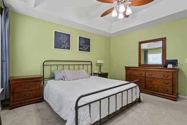 bedroom with ceiling fan, a raised ceiling, and light colored carpet