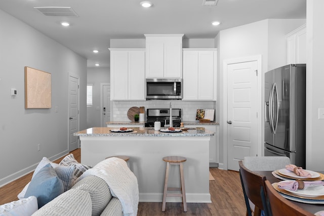 kitchen with stainless steel appliances, a center island with sink, light stone countertops, white cabinets, and dark hardwood / wood-style flooring