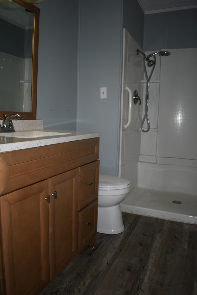 bathroom featuring toilet, hardwood / wood-style flooring, ornamental molding, vanity, and a shower