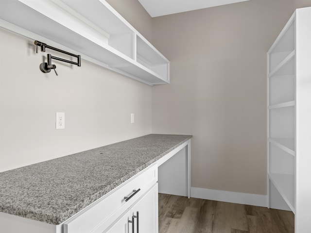 interior space with white cabinets, light hardwood / wood-style floors, light stone countertops, and built in desk