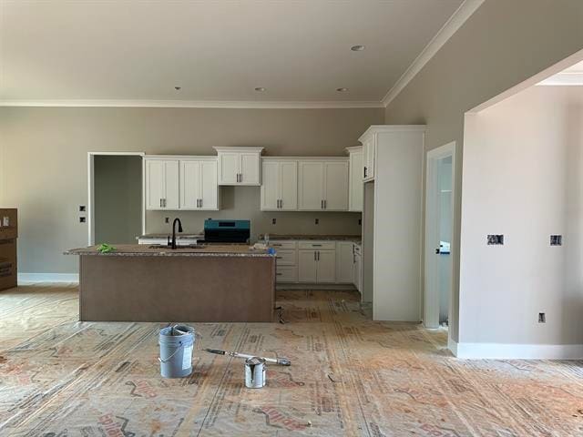 kitchen featuring crown molding, dark stone counters, white cabinetry, sink, and a kitchen island with sink